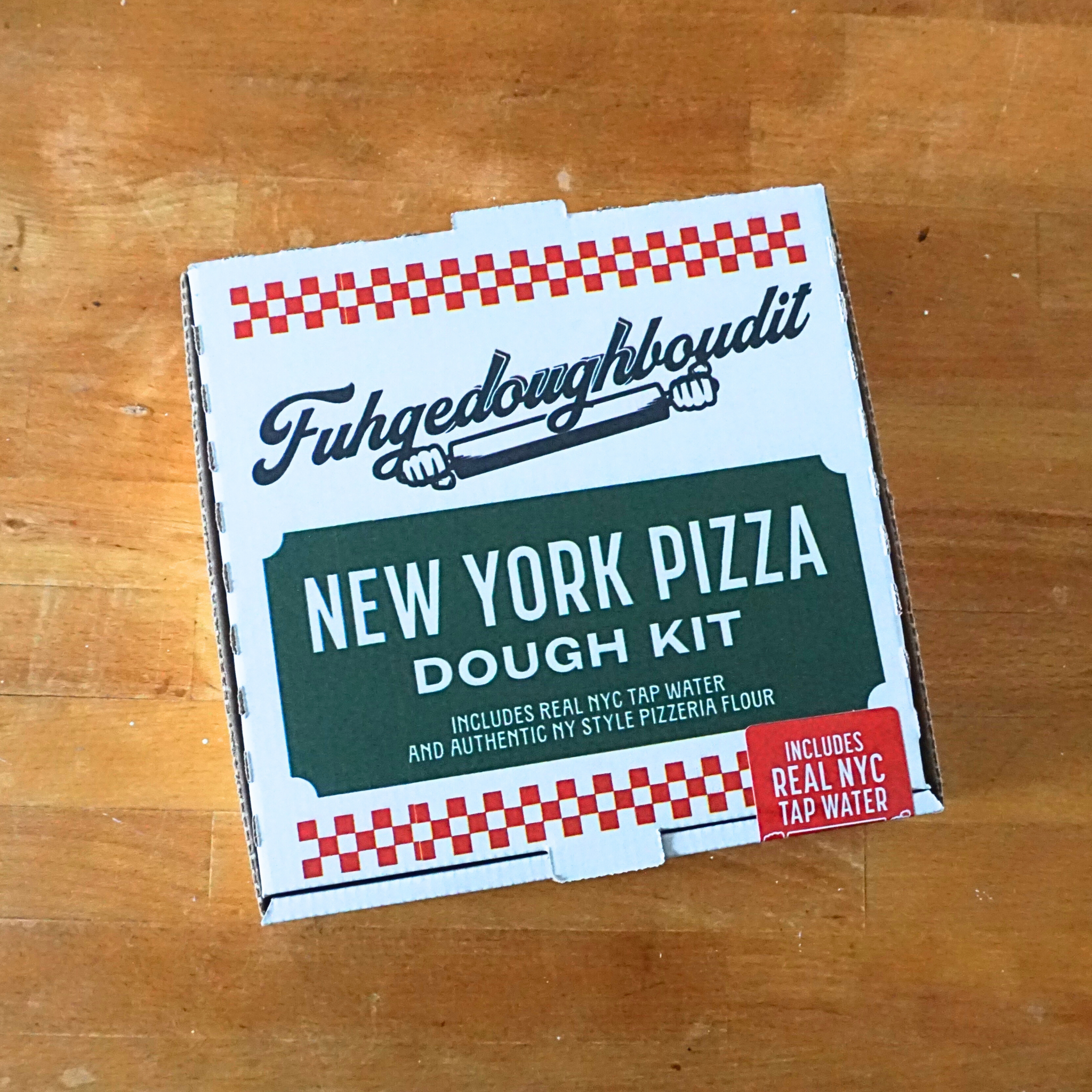 A packaged New York Pizza Dough Kit by Fuhgedoughboudit, with branding and text indicating the product includes real NYC tap water and authentic NY style flour.