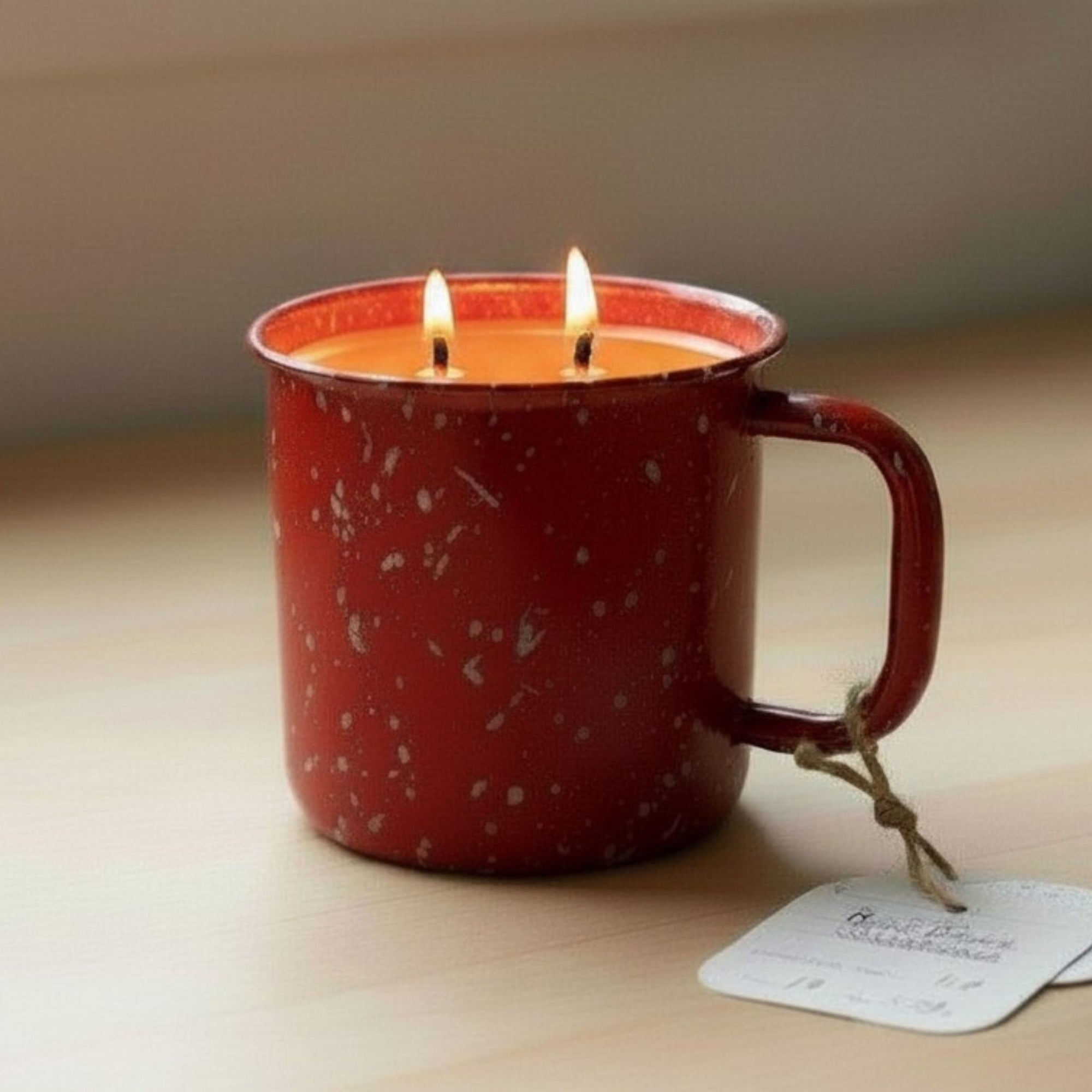Red speckled mug with two lit candles on a wooden surface
