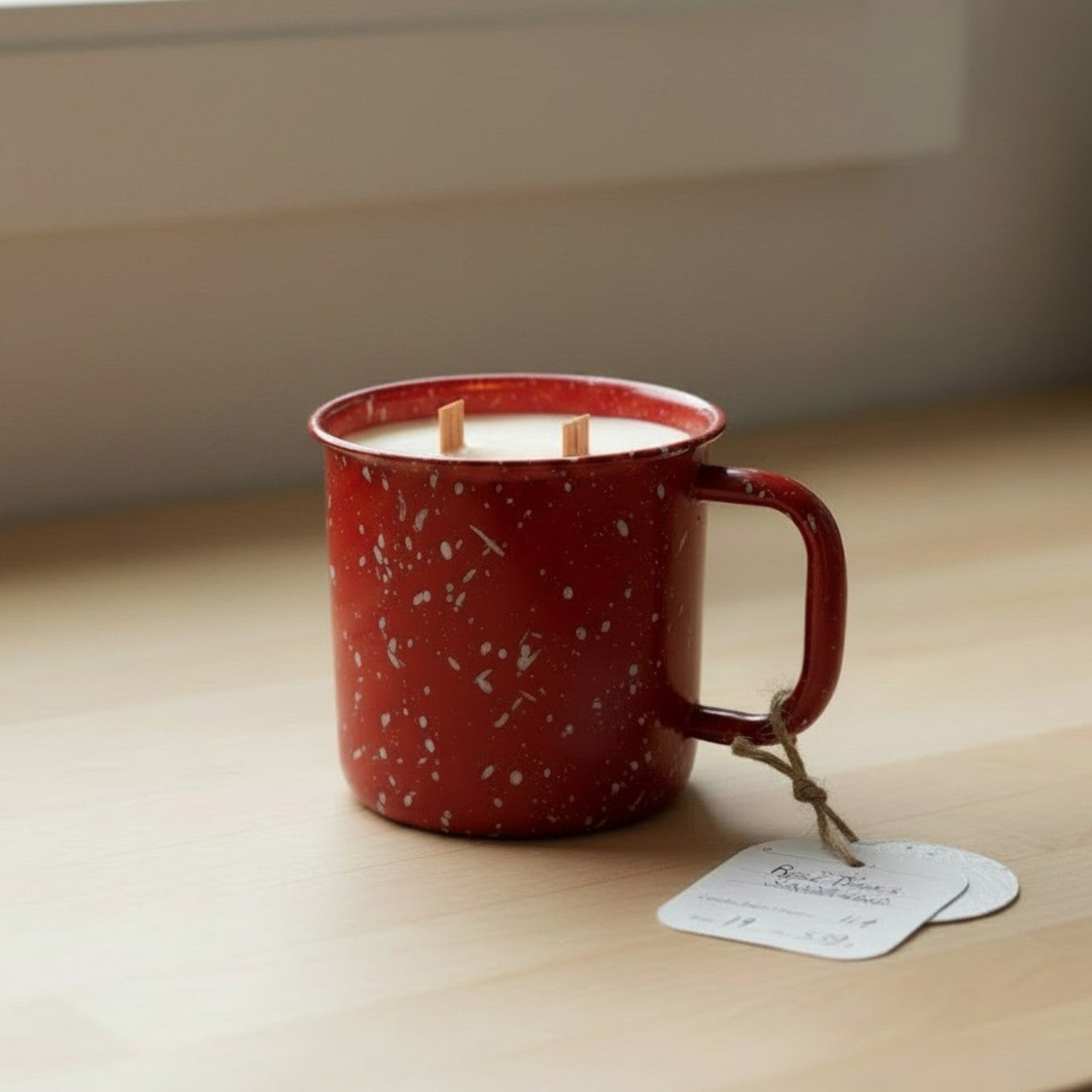 Red speckled mug with a candle inside on a wooden surface near a window.