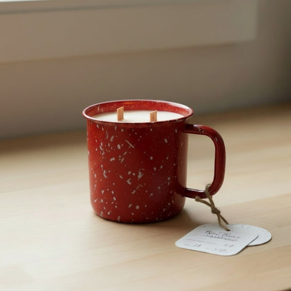 Red speckled mug with a candle inside on a wooden surface near a window.