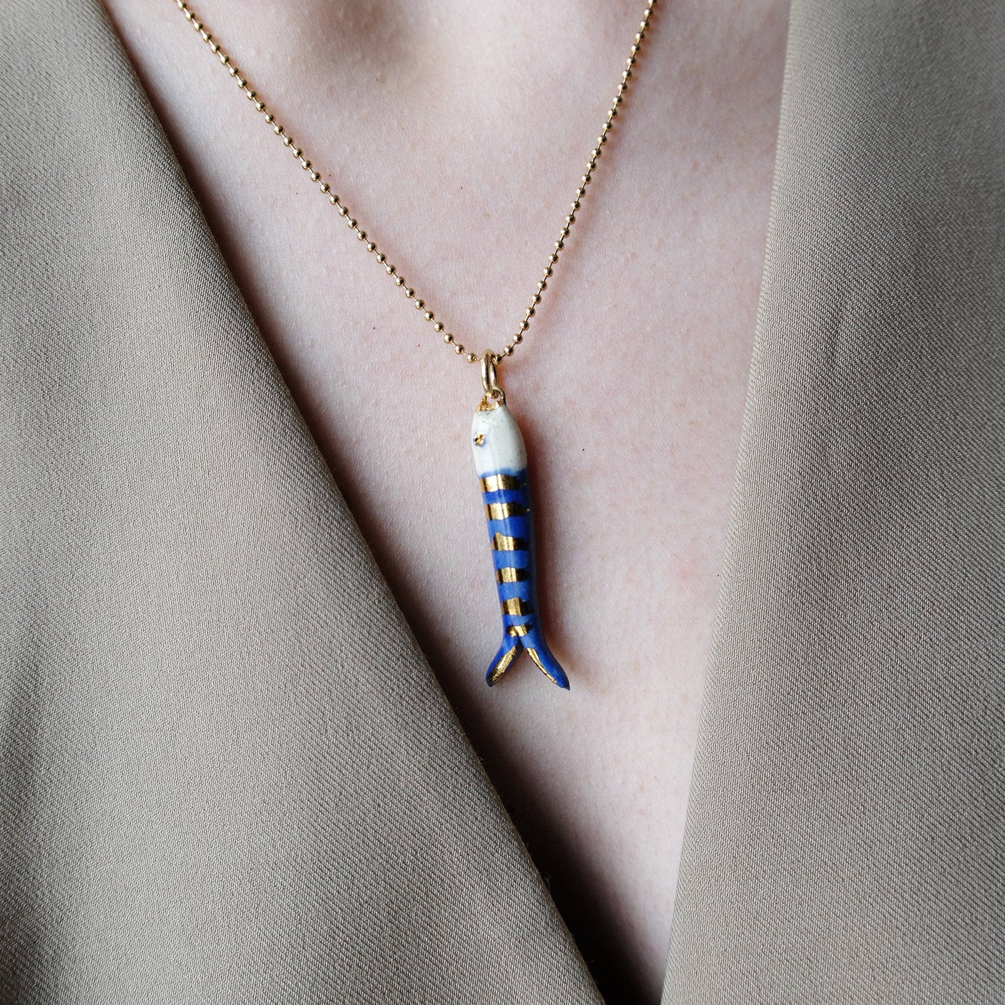 Necklace with a fish-shaped pendant worn by a person in a neutral setting