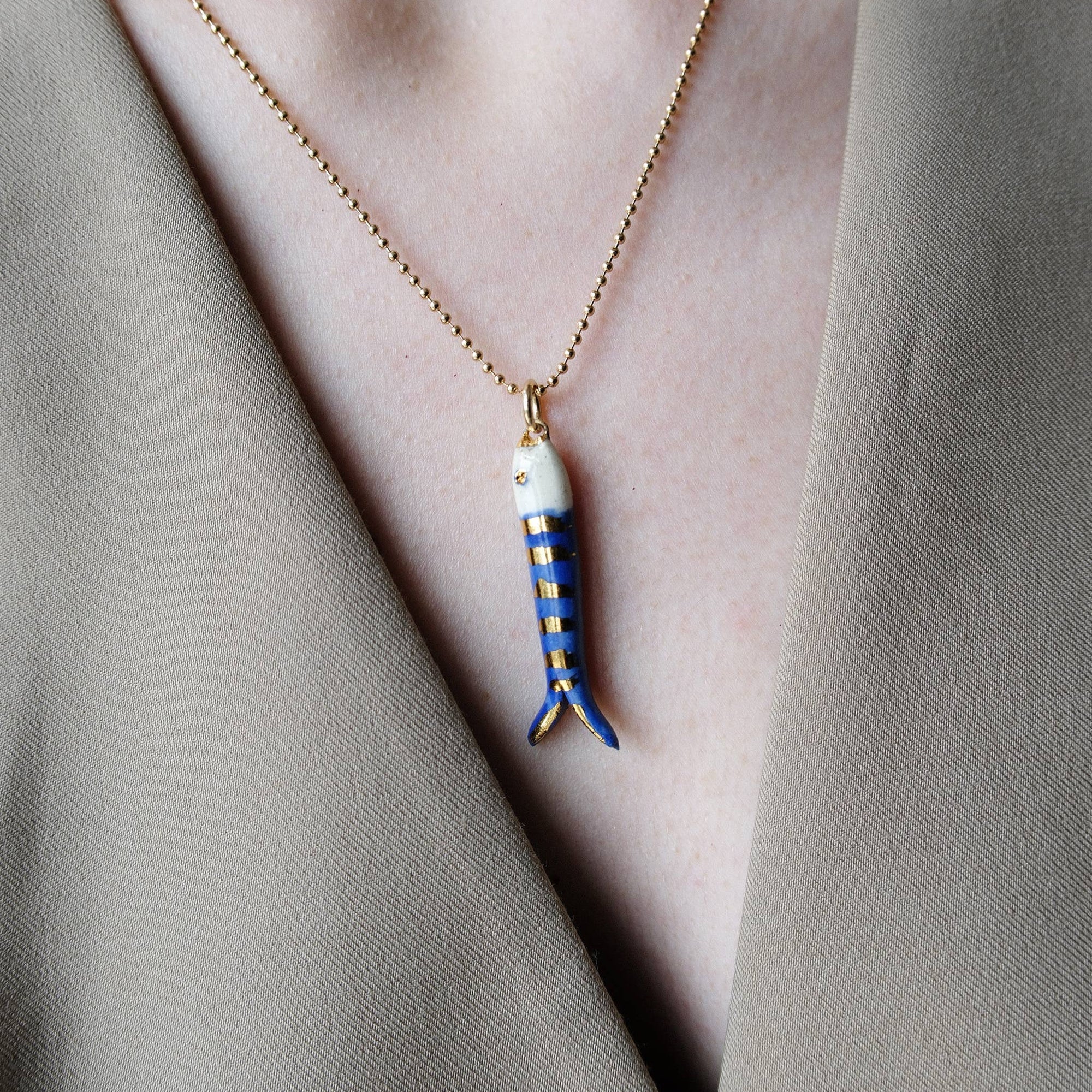 Necklace with a fish-shaped pendant worn by a person in a neutral setting