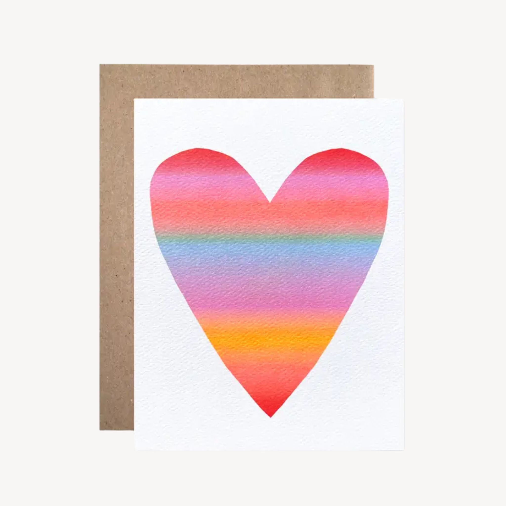 A white greeting card with a large watercolor heart in pink, orange, yellow, and blue stripes, shown with a brown kraft envelope on a light beige background.