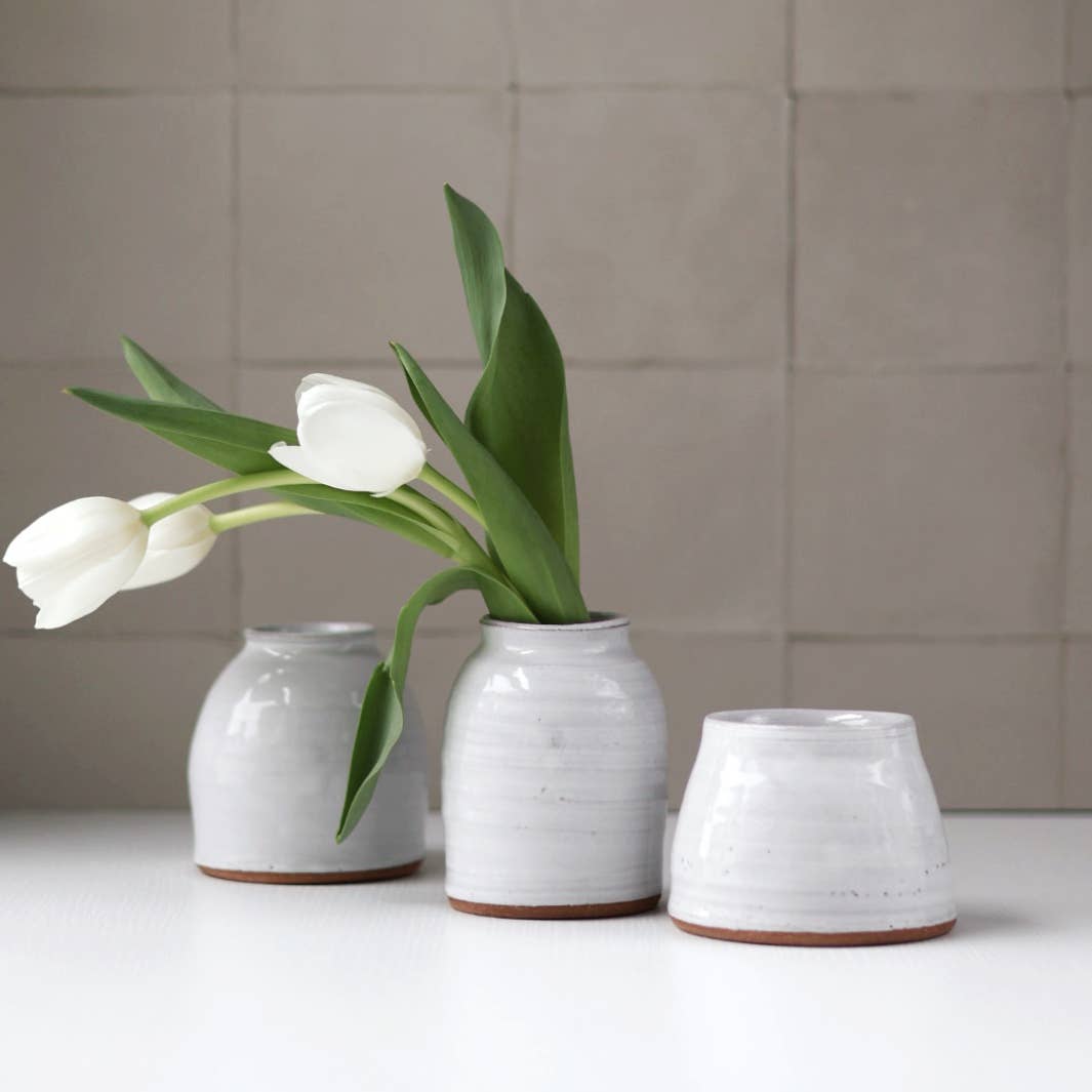 Three white ceramic vases with a single white tulip on a neutral background