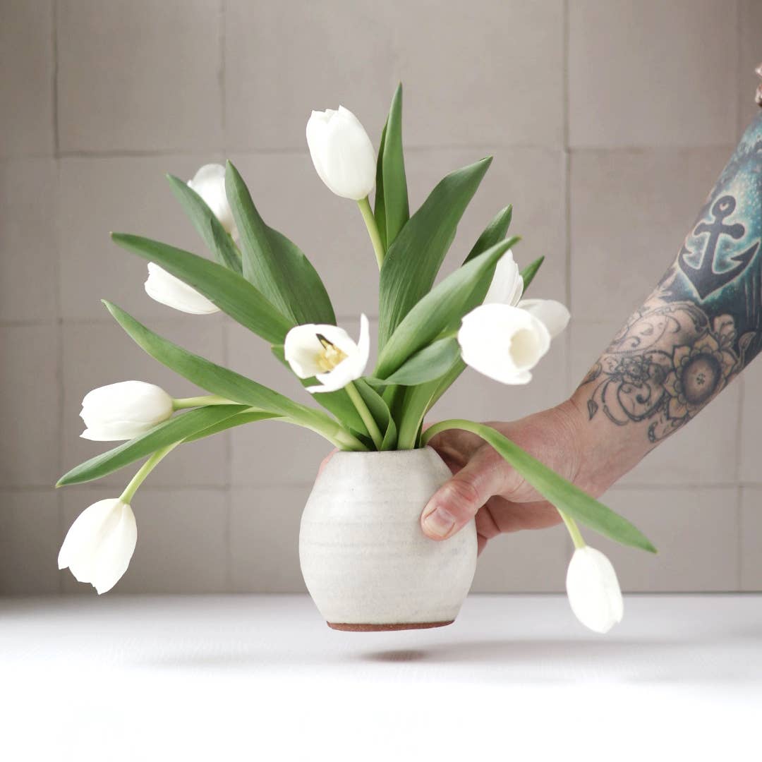 Person holding a white ceramic vase with white tulips against a neutral background