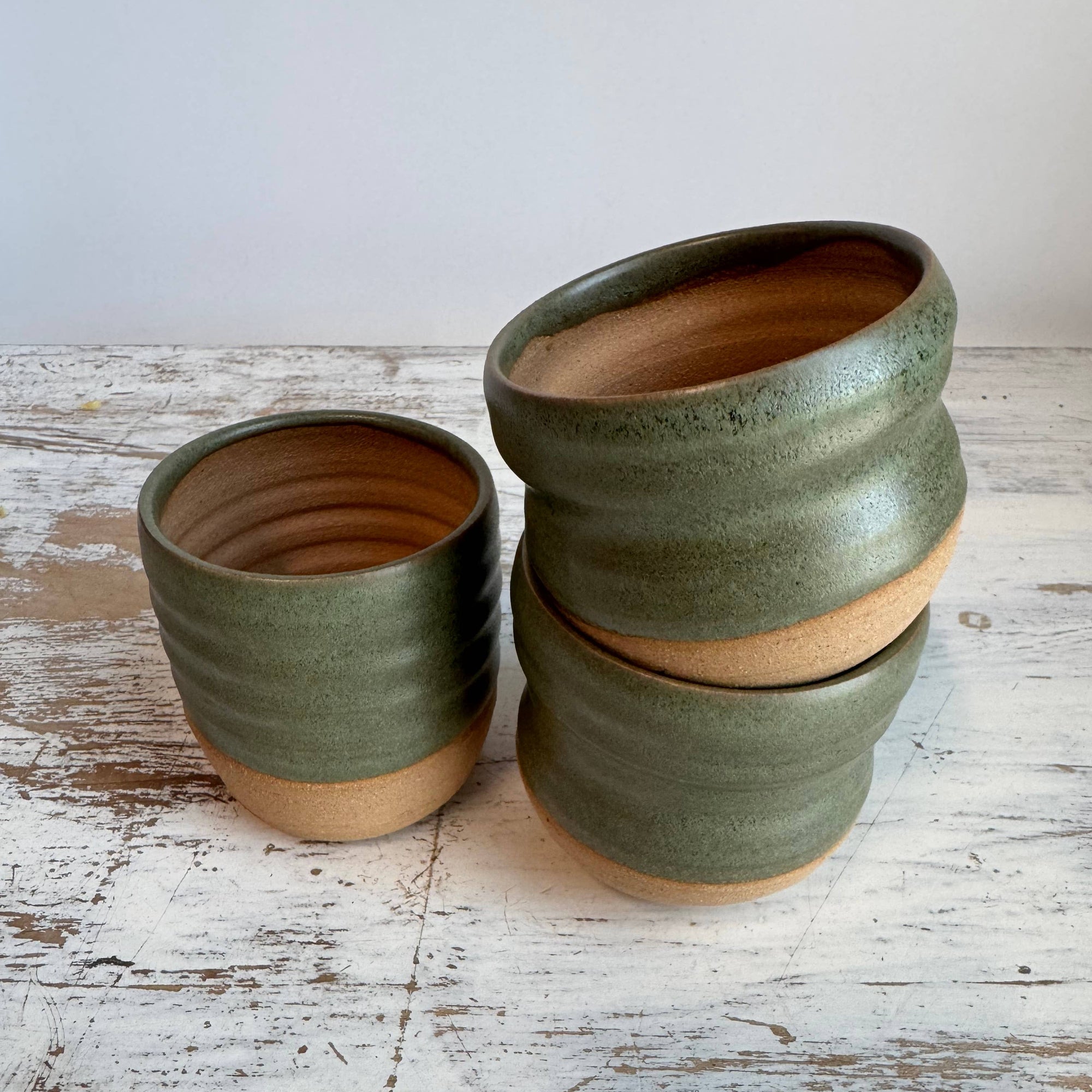 Three green ceramic planters stacked on a wooden surface