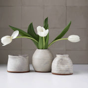 Three ceramic vases with white tulips on a neutral background