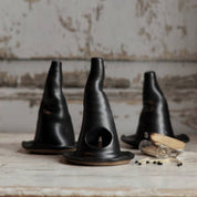 Three black ceramic black witch's hats on a rustic wooden surface with a textured wall background.