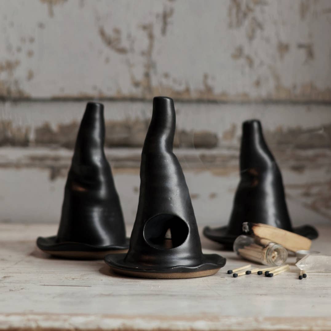 Three black ceramic black witch's hats on a rustic wooden surface with a textured wall background.