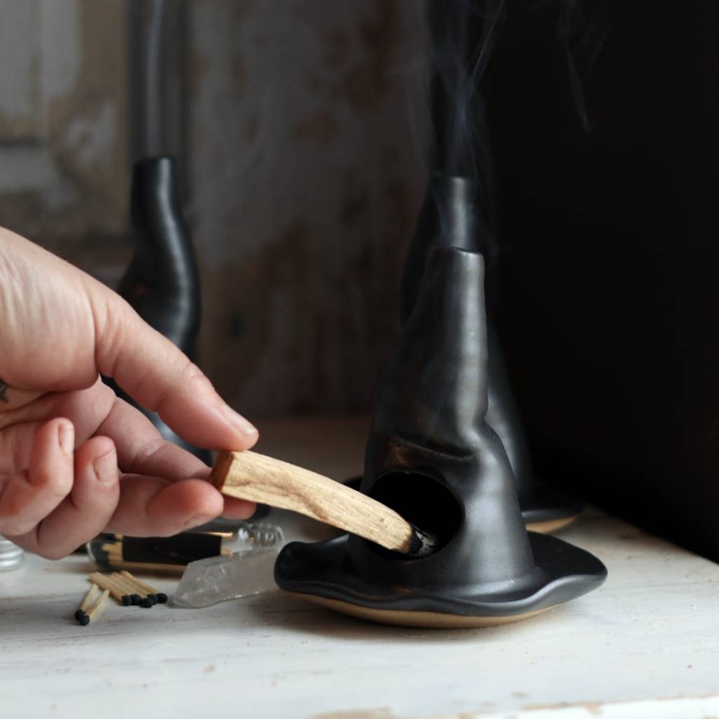 Person placing a wooden stick into a black ceramic object on a marble surface.