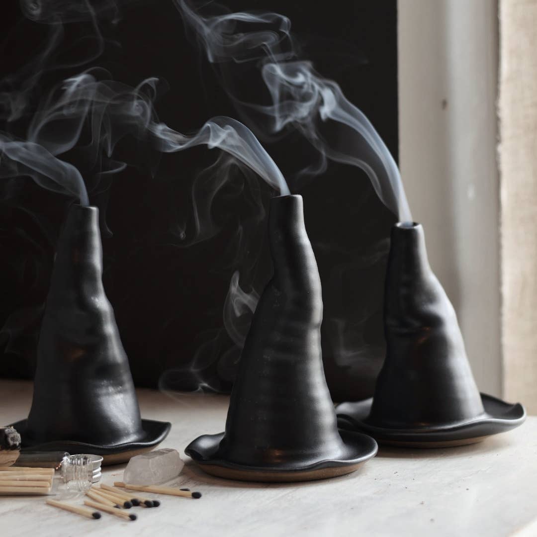Black ceramic incense burners with smoke on a light surface.
