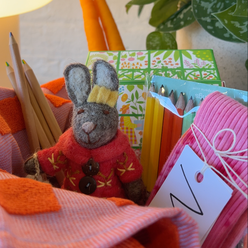 Small plush rabbit toy in a red sweater with a yellow hat, surrounded by colorful pencils and stationery items.