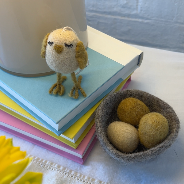 Small bird figurine on a stack of colorful books with a bowl of eggs on a white surface.