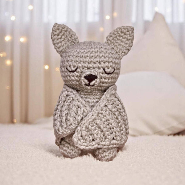 Crocheted bat toy on a soft surface with blurred lights in the background