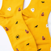 Bright yellow crew socks with a Halloween pattern featuring black bats, orange jack-o'-lanterns, white ghosts, and black spiders, laid flat on a white background.