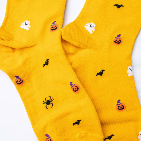 Bright yellow crew socks with a Halloween pattern featuring black bats, orange jack-o'-lanterns, white ghosts, and black spiders, laid flat on a white background.