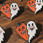 Halloween-themed pins with ghosts and pumpkins on a wooden surface.