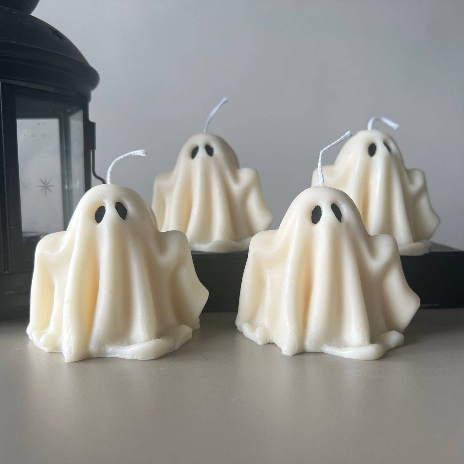 Ghost-shaped candles on a table with a lantern in the background