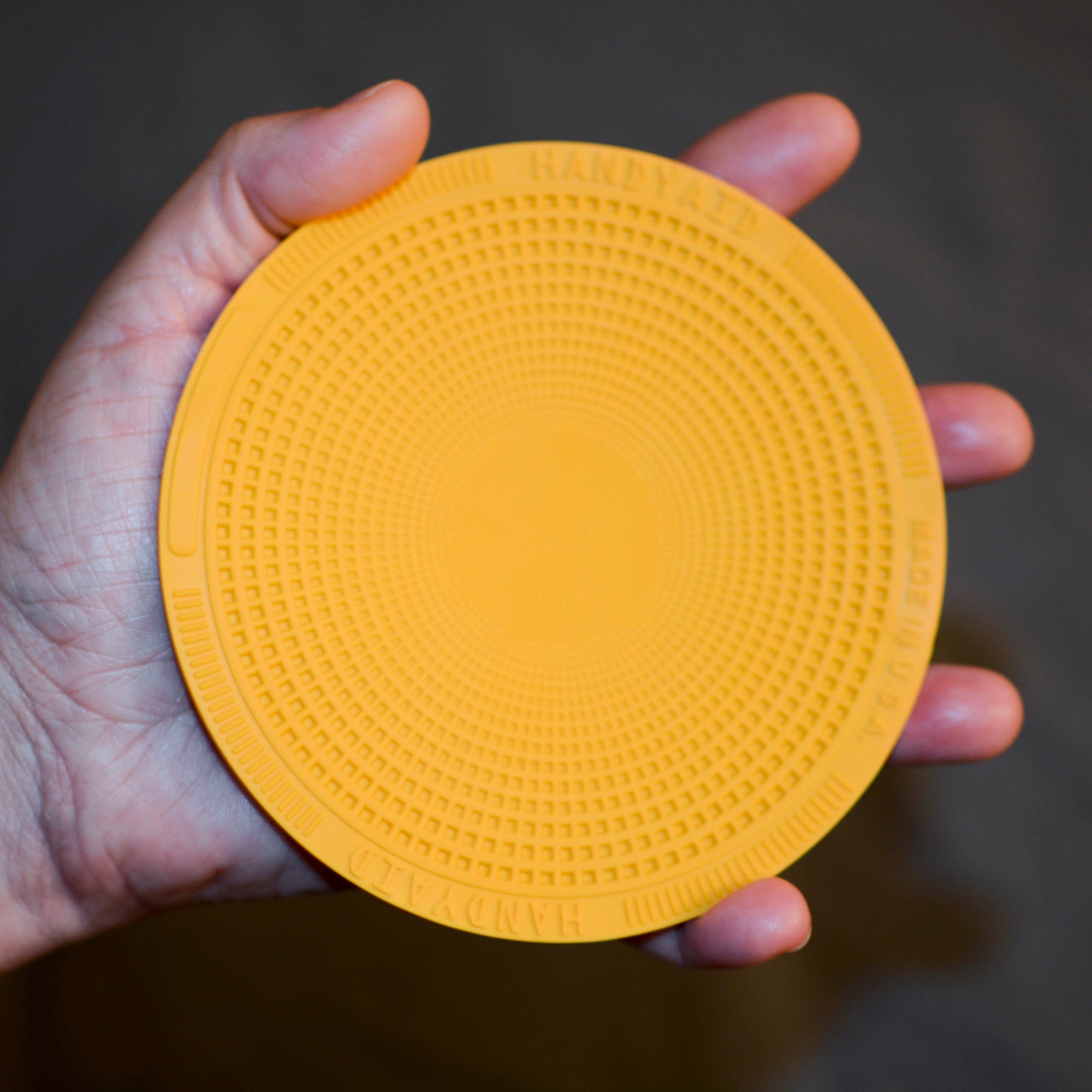 Hand holding a yellow textured circular object against a dark background