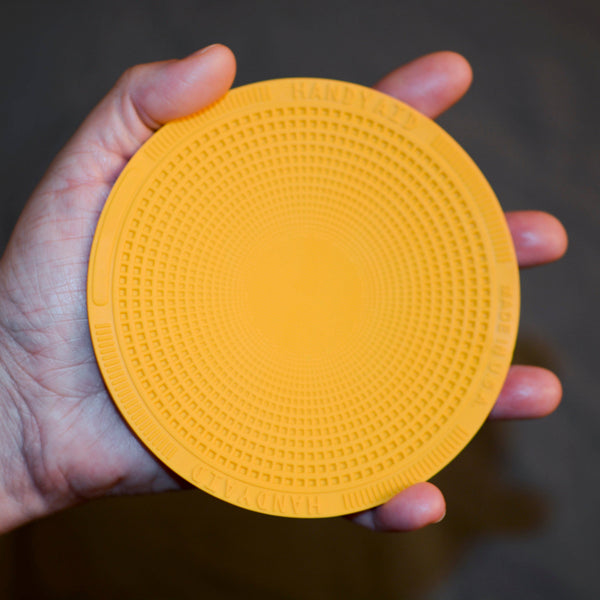 Hand holding a yellow textured circular object against a dark background