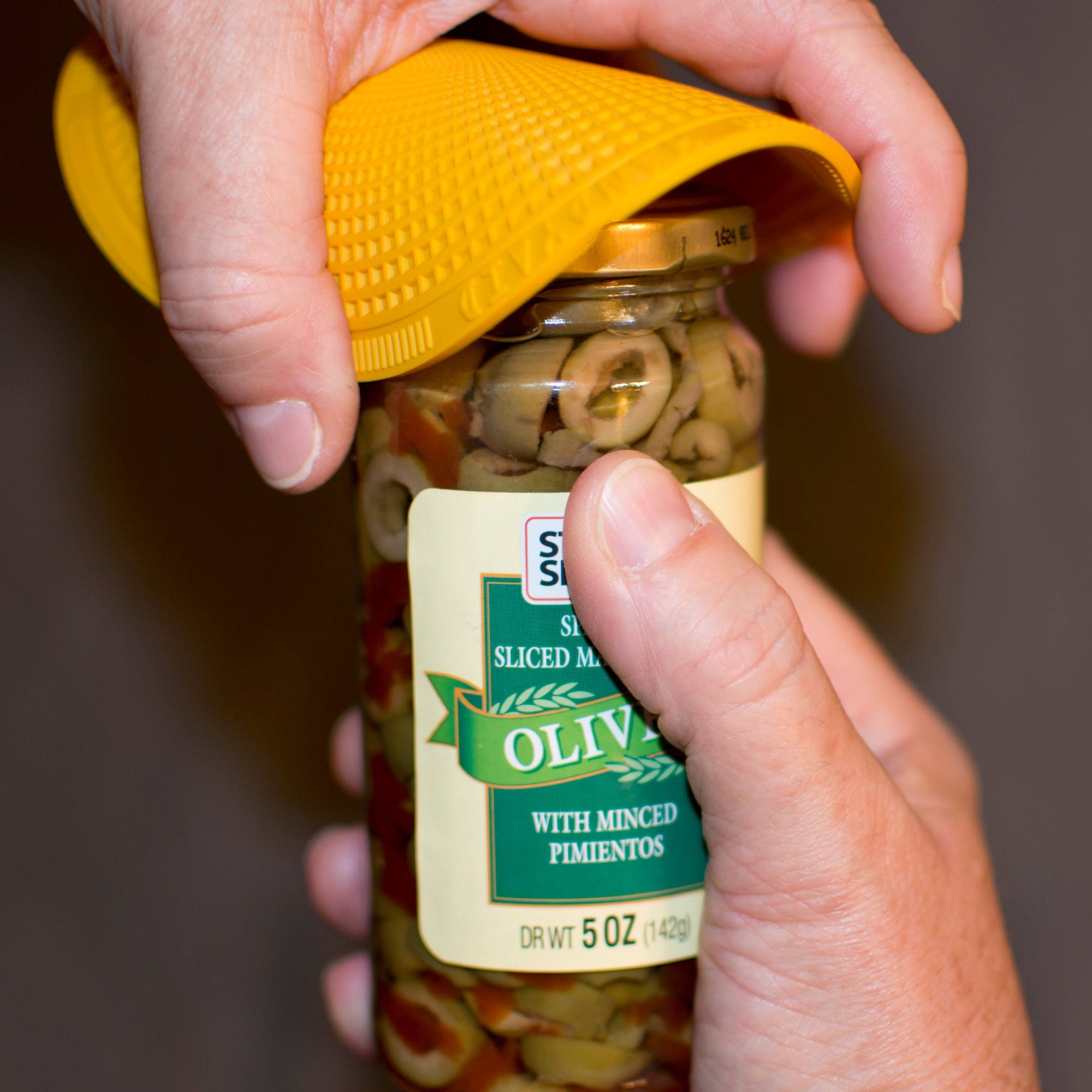 Hand holding a jar of sliced olives with a yellow lid.