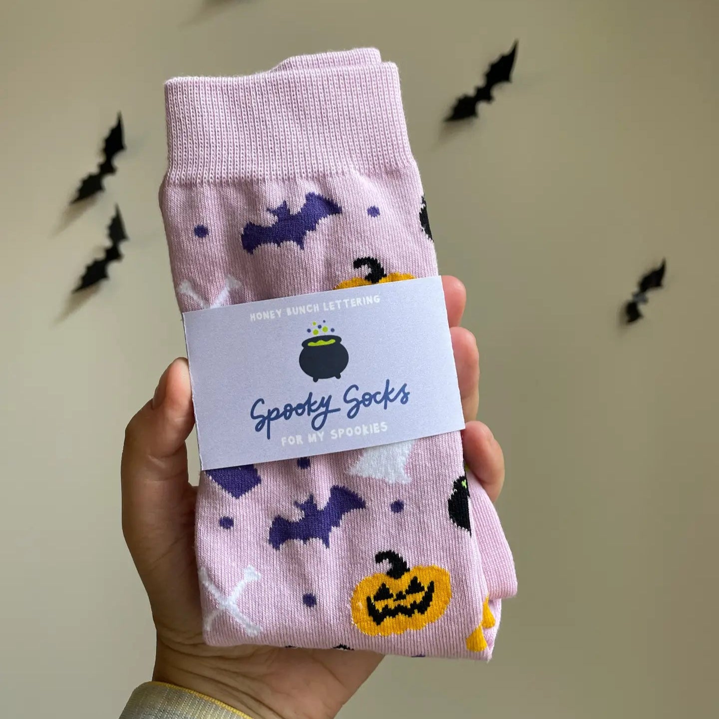 Spooky socks with Halloween designs held by a hand against a neutral background with decorative bats.