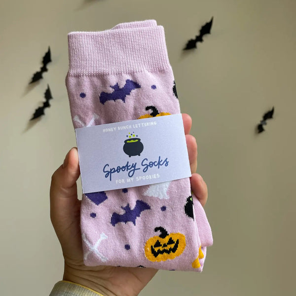Spooky socks with Halloween designs held by a hand against a neutral background with decorative bats.