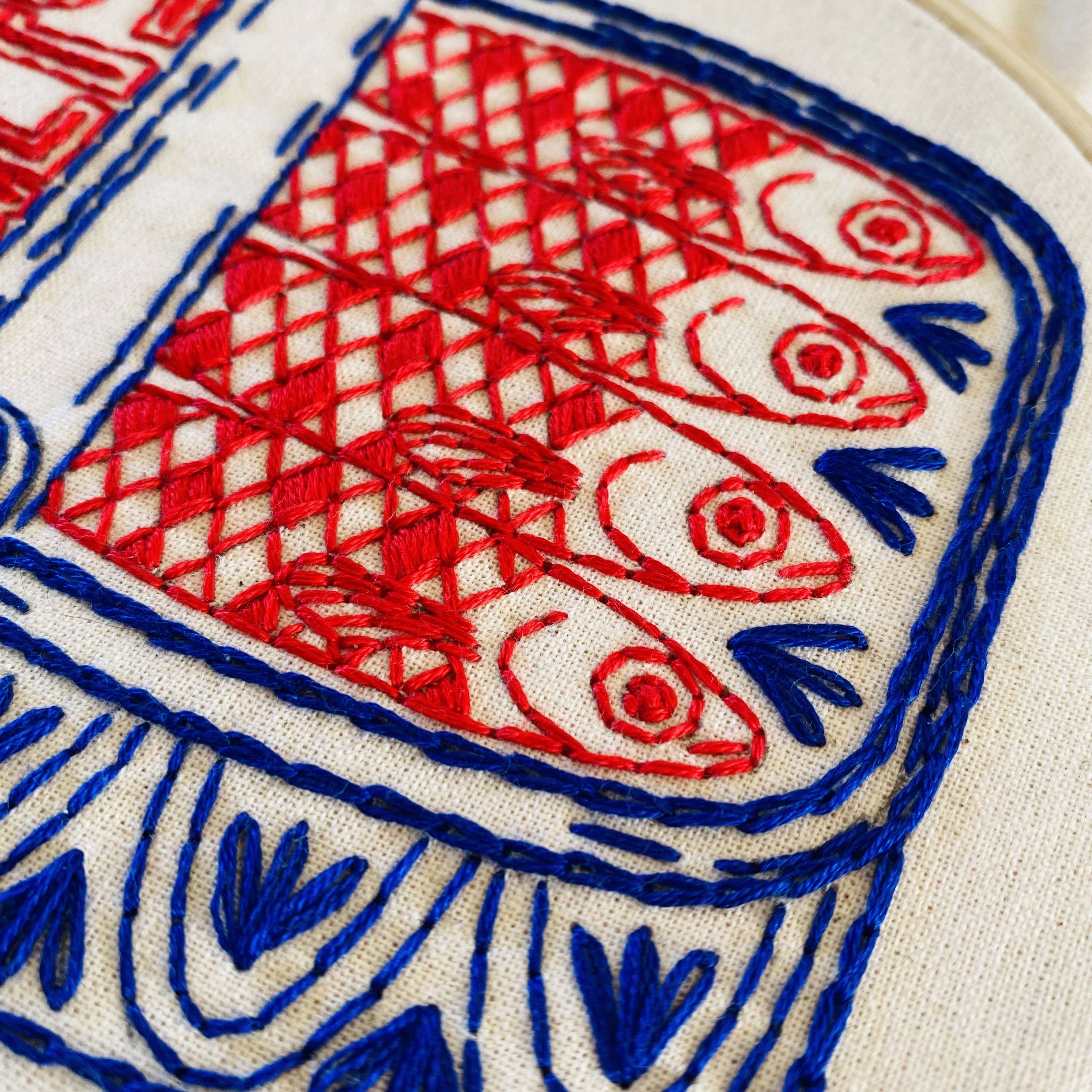 Embroidered design with red and blue fish on a white fabric background