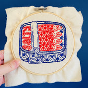 Embroidery hoop with red and blue pattern on beige fabric against a blue background