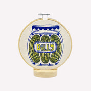 Embroidery hoop with a design of pickles in a jar labeled 'Dilly' on a white background