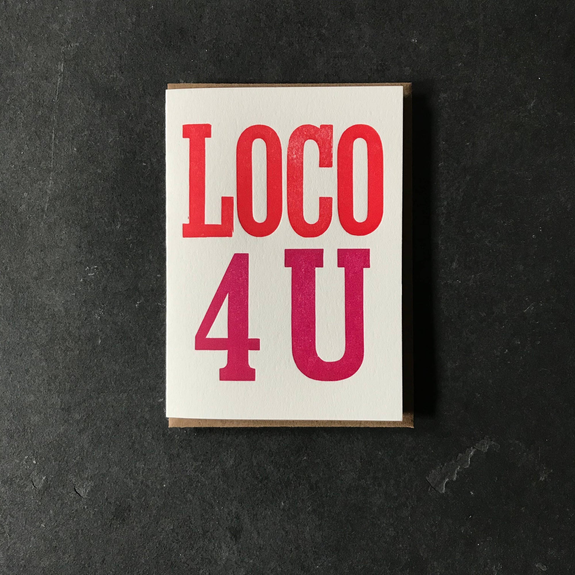 A greeting card with 'Loco 4 U' printed in red and pink on a white background, placed on a dark background.