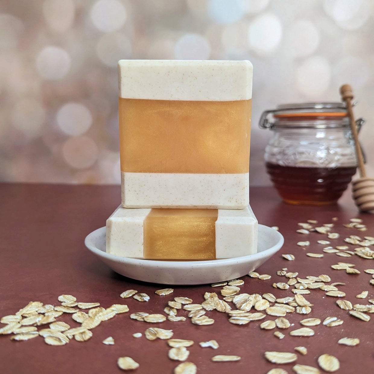 Two layered soap bars on a white plate with oats and a jar of honey in the background.