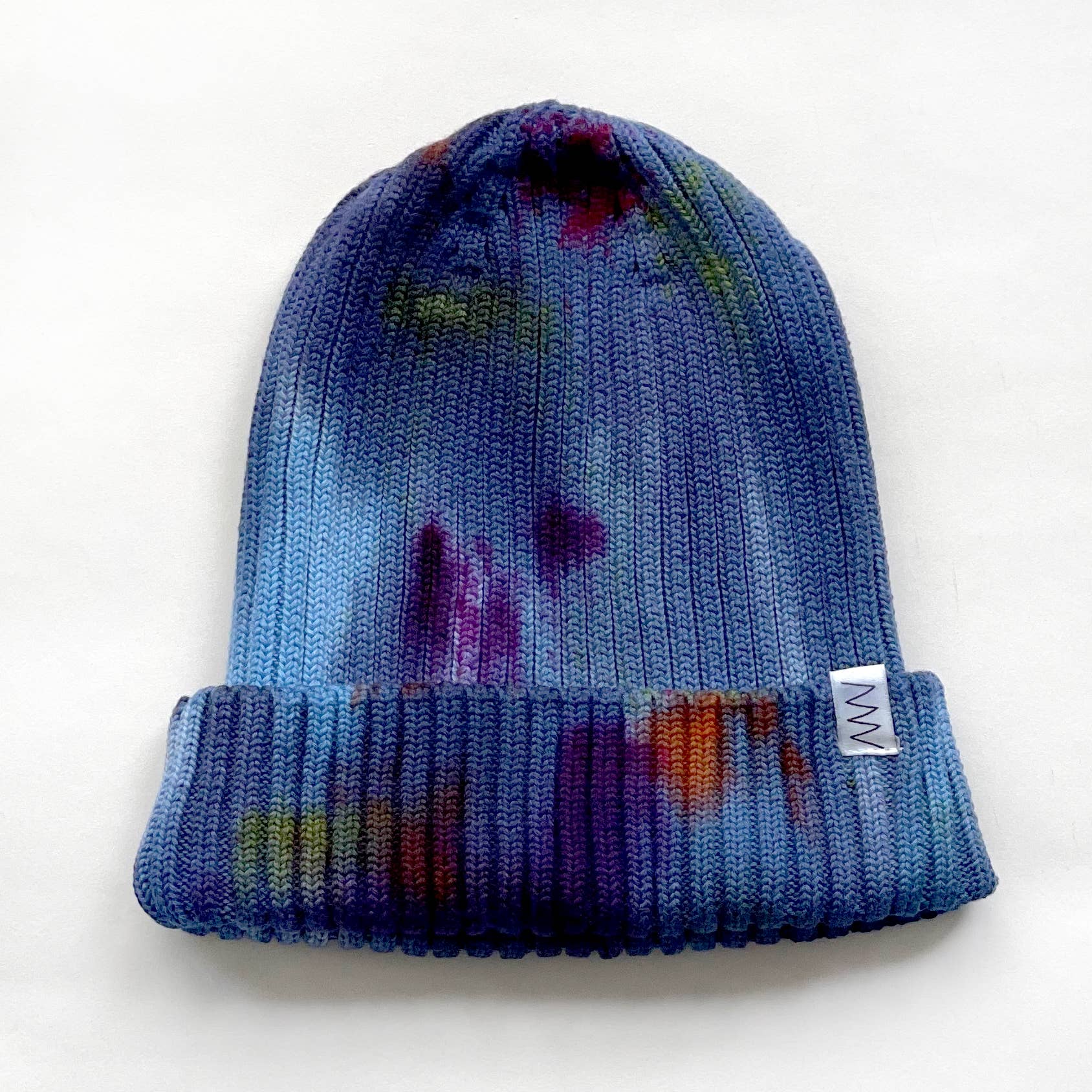 A hand dyed blue beanie hat against a white background.