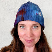 A woman wearing a hand dyed blue beanie hat standing against a white background.