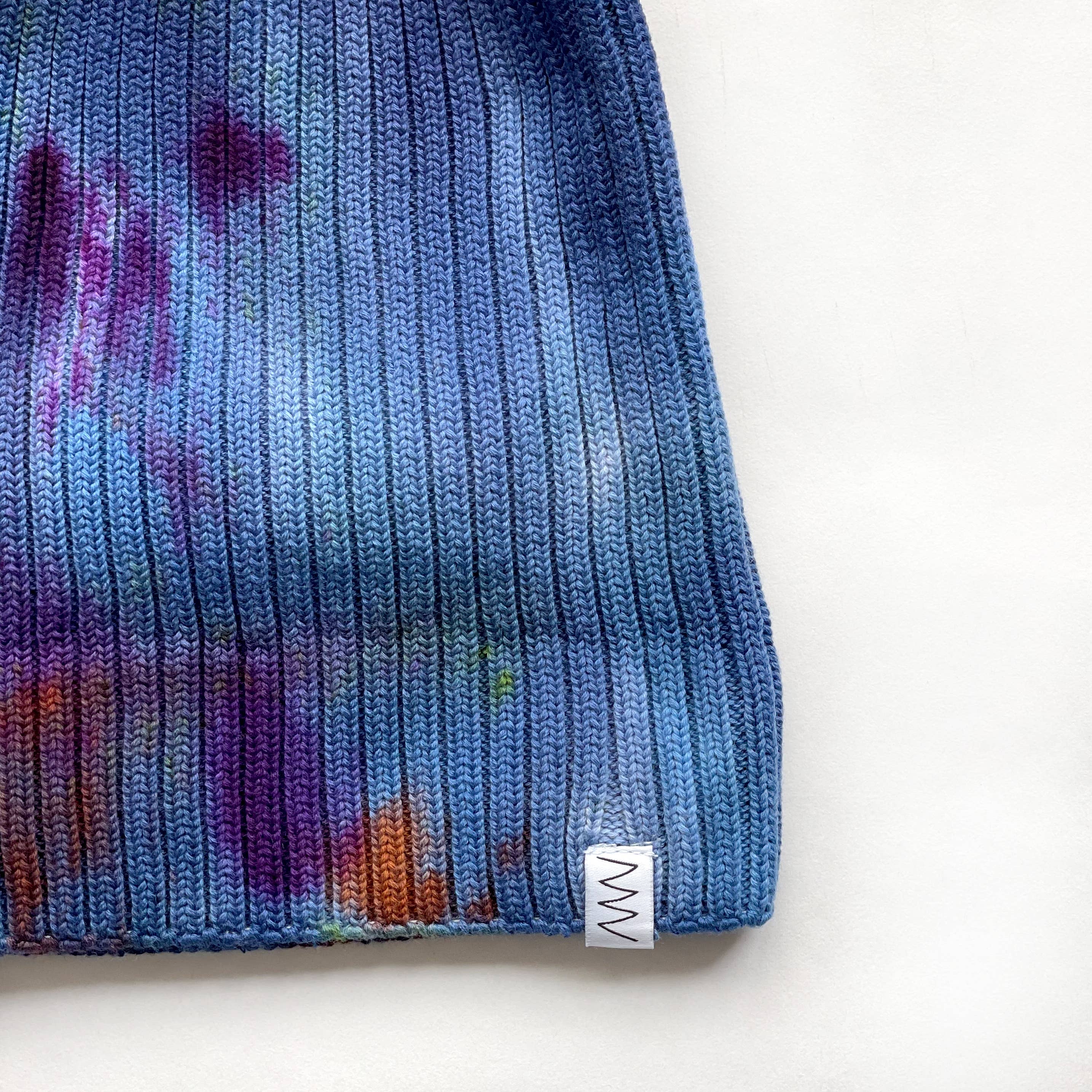 The detail of a blue beanie hat against a white background.