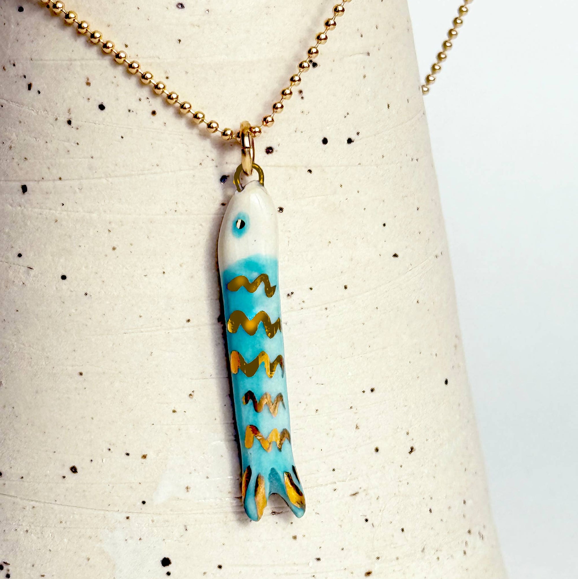 Fish-shaped pendant on a necklace against a speckled background