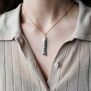 Necklace with a fish pendant worn by a person in a light-colored shirt.