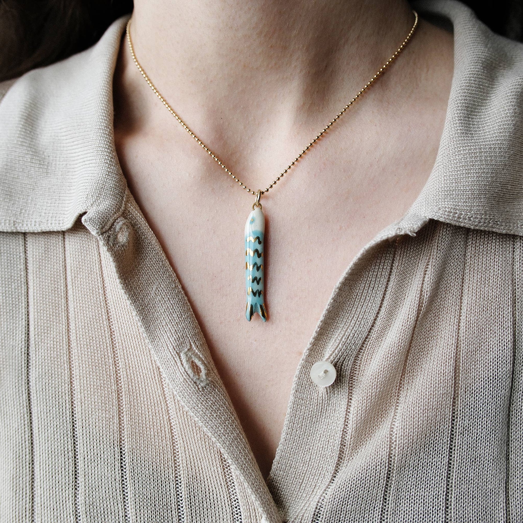 Necklace with a fish pendant worn by a person in a light-colored shirt.