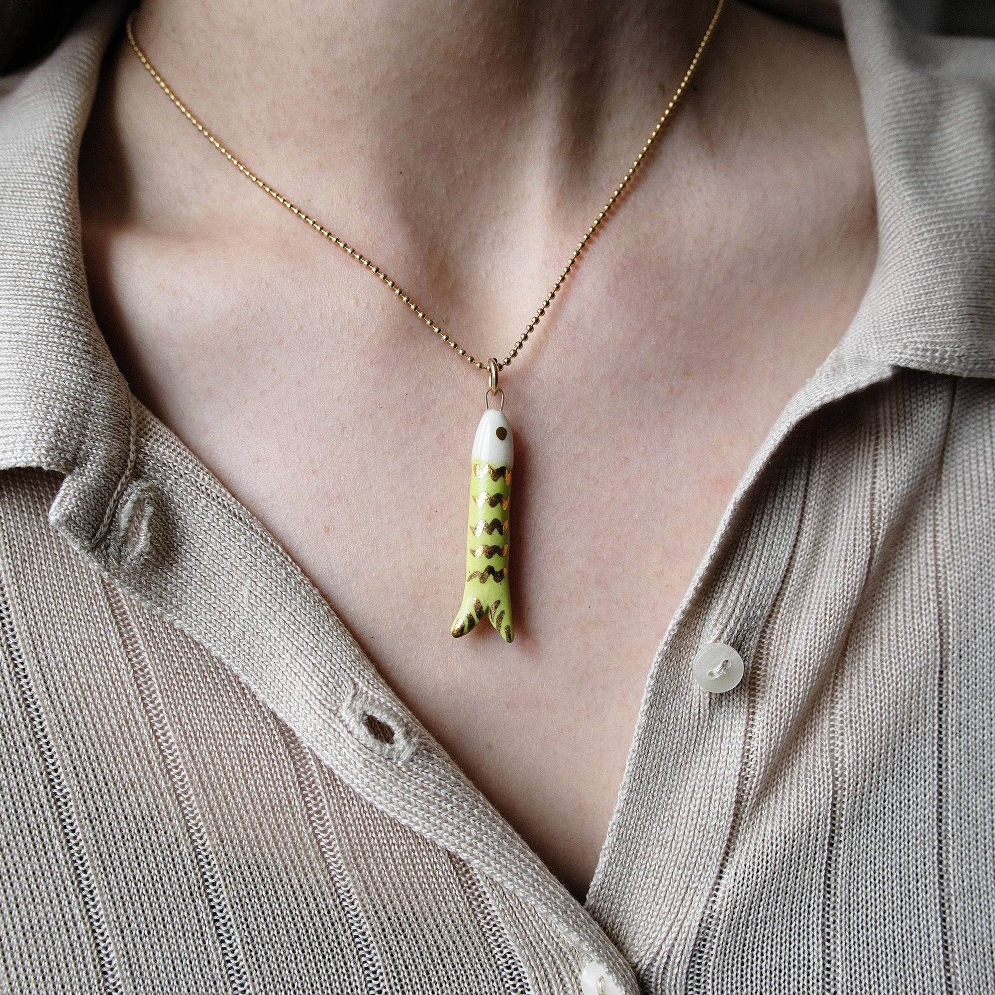 Necklace with a fish pendant worn by a person in a light-colored shirt.