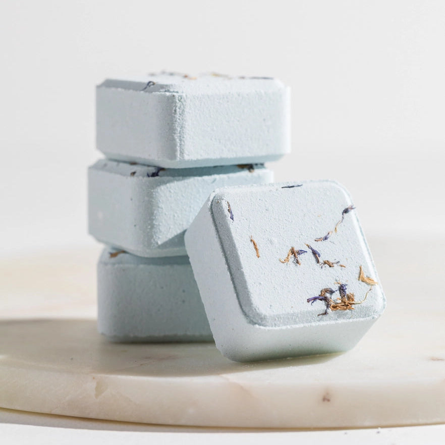 Stack of light blue shower steamer squares with a floral pattern on a white surface
