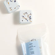 Two small containers with floral designs on lids and a package of 'Mist' product on a light background.
