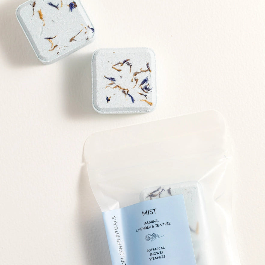 Two small containers with floral designs on lids and a package of 'Mist' product on a light background.