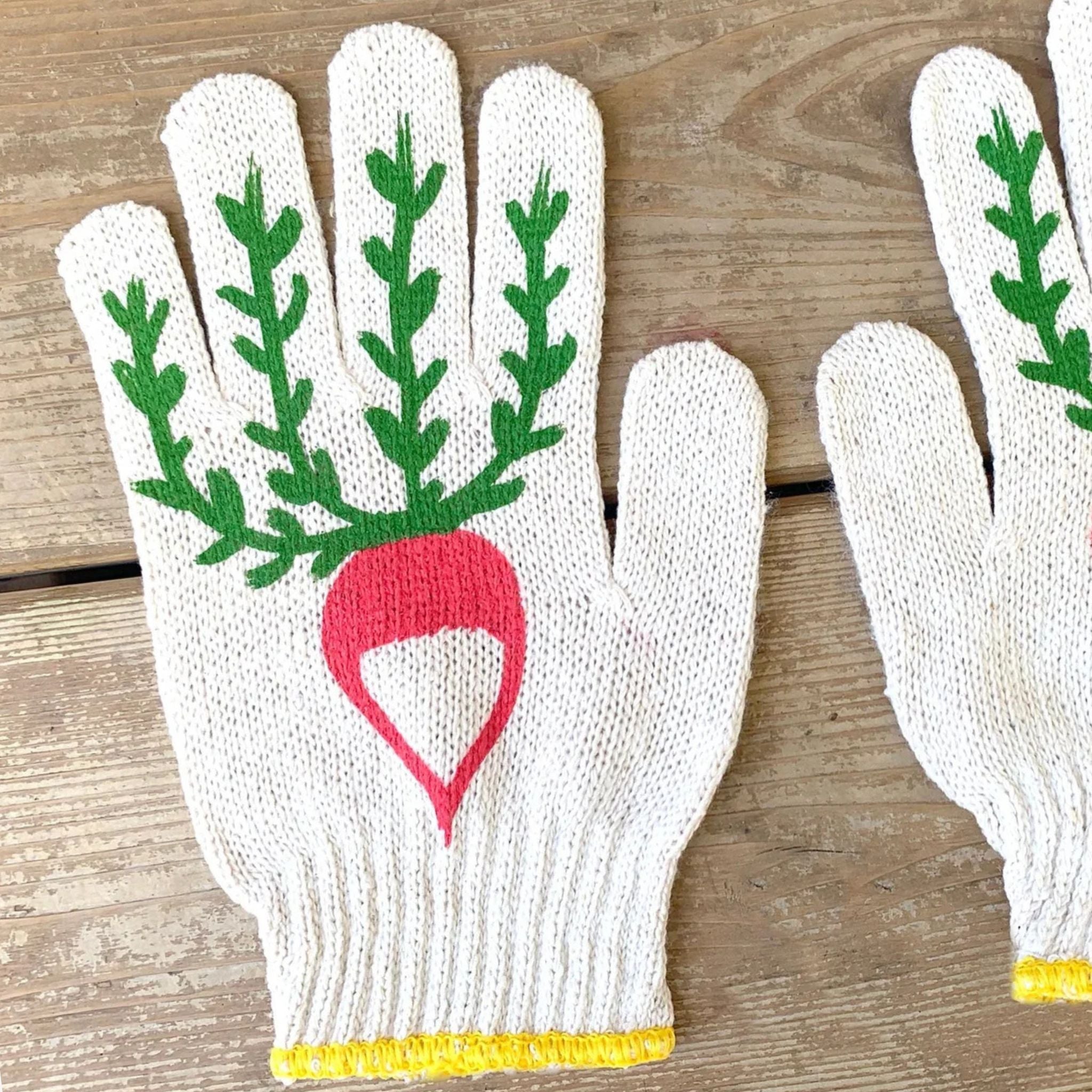 White gloves with green leaf design and red heart on a wooden surface