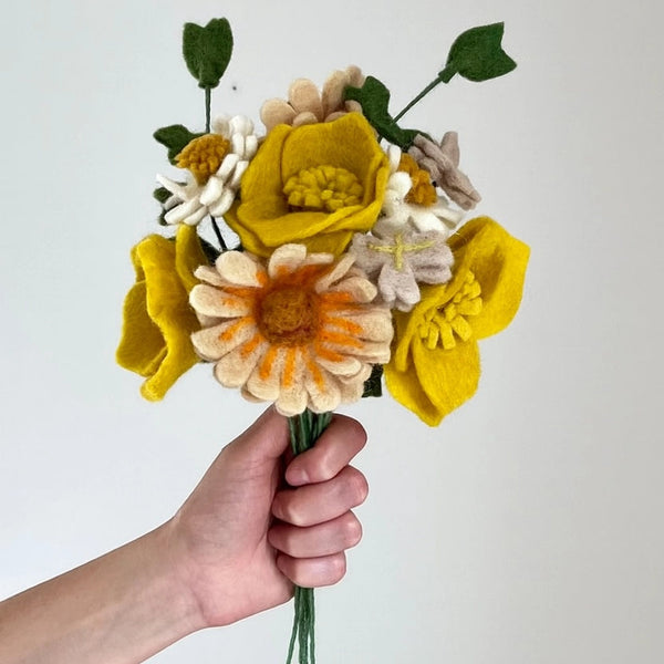 Hand holding a bouquet of felt flowers against a plain background