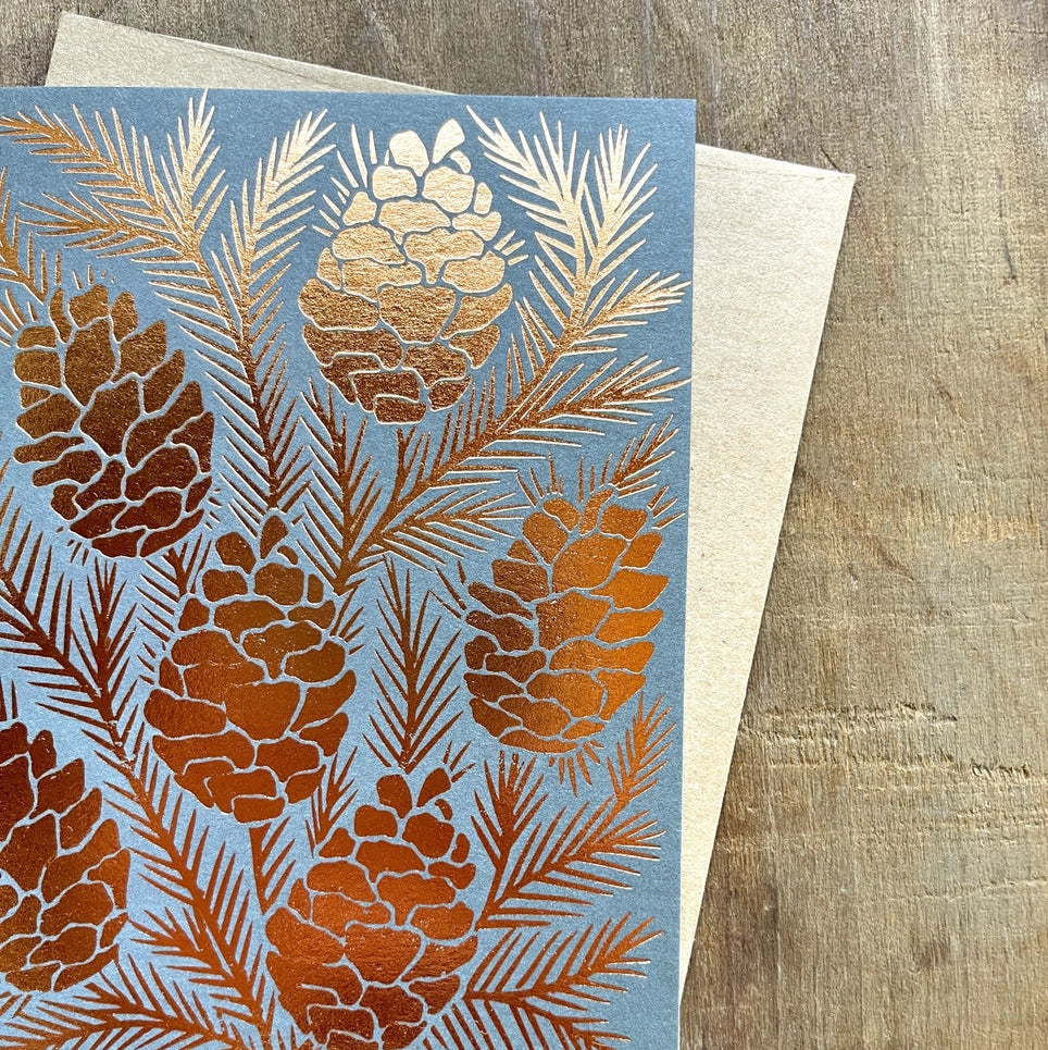 Greeting card with pine cone and branch design on a wooden surface