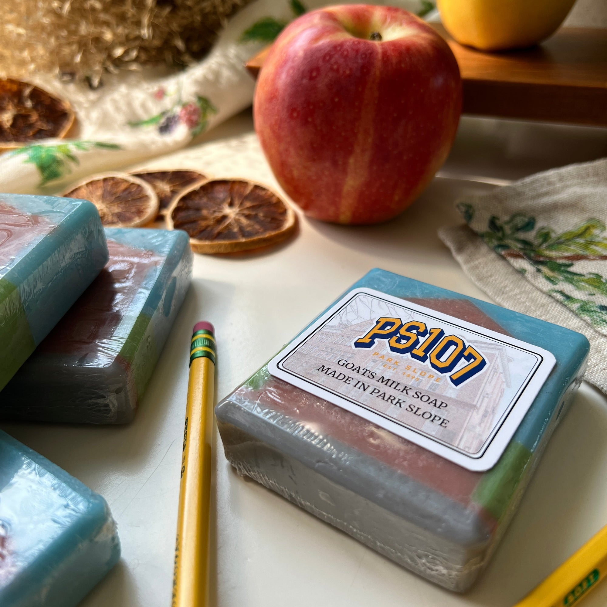 Bar of soap with a label, lemon, apple, and pencil on a textured surface