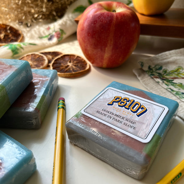 Bar of soap with a label, lemon, apple, and pencil on a textured surface