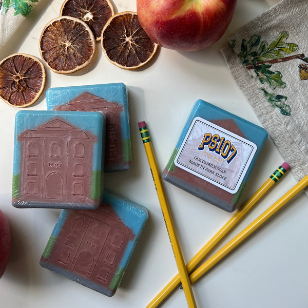 Three bars of soap with decorative designs on a white surface, surrounded by an apple, dried fruit, and pencils.