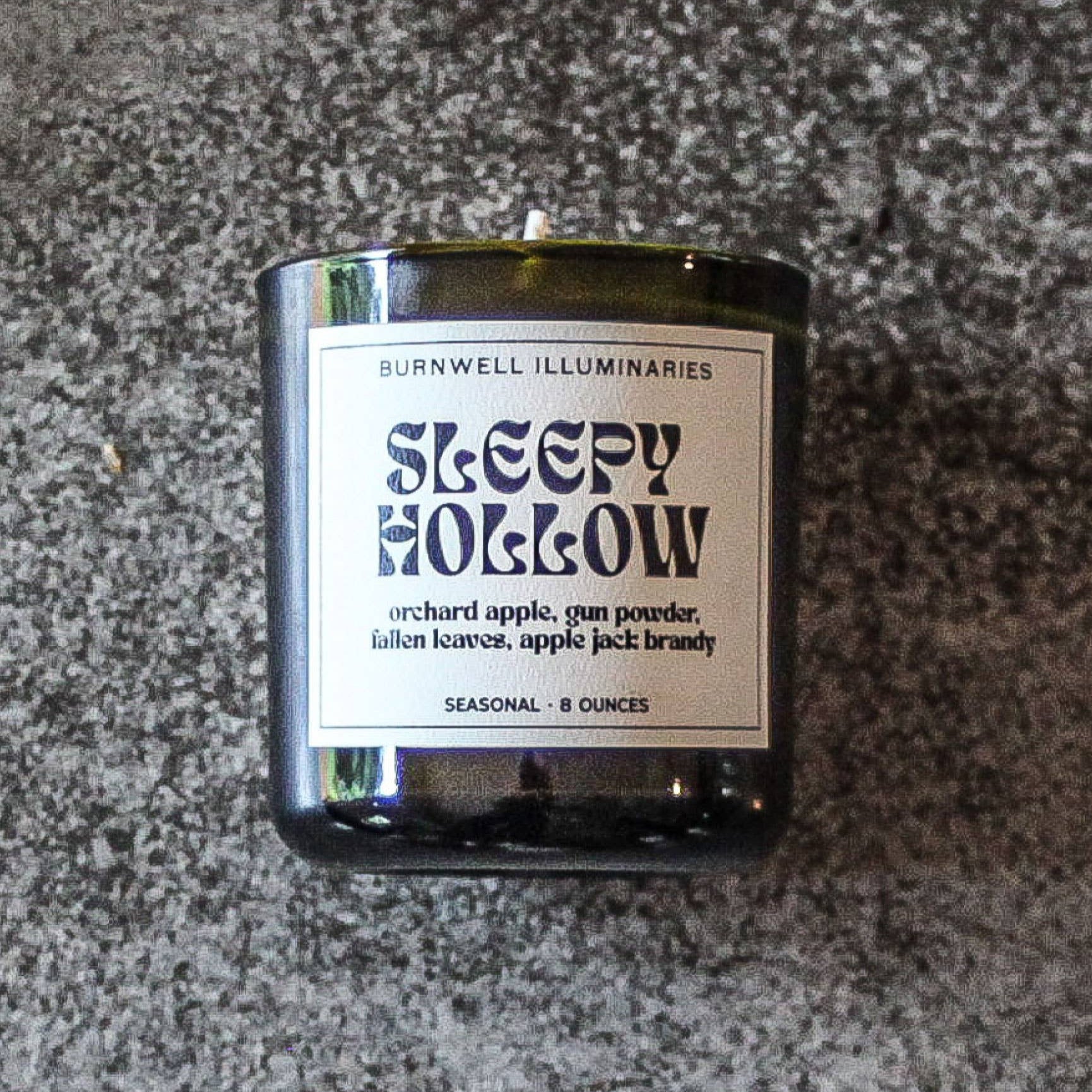 Candle labeled 'Sleepy Hollow' by Burnwell Illuminaries on a textured surface