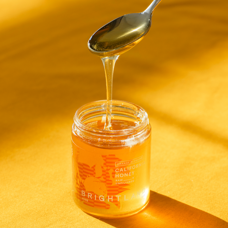 Jar of honey with a spoon dripping honey on a yellow background